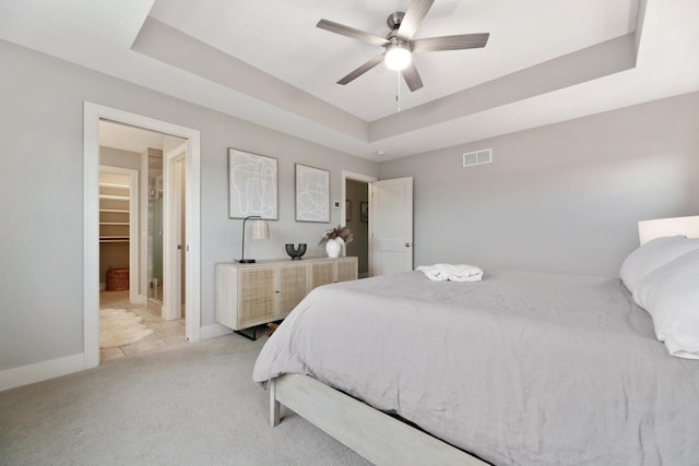 bedroom featuring light carpet, baseboards, visible vents, a raised ceiling, and a ceiling fan