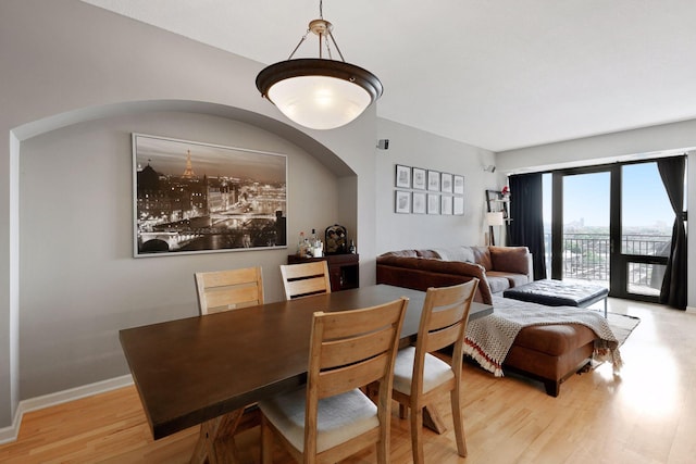 dining space featuring arched walkways, baseboards, and light wood finished floors