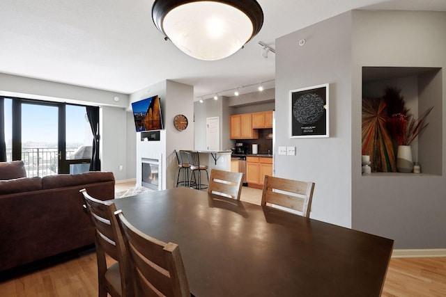 dining room featuring light wood-type flooring, baseboards, track lighting, and a glass covered fireplace