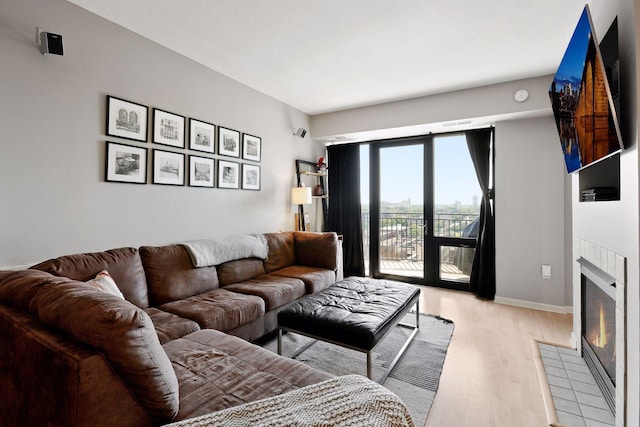 living room featuring baseboards, light wood-style flooring, and a tiled fireplace