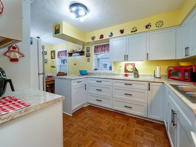 kitchen featuring light countertops, freestanding refrigerator, white cabinetry, a textured ceiling, and a peninsula