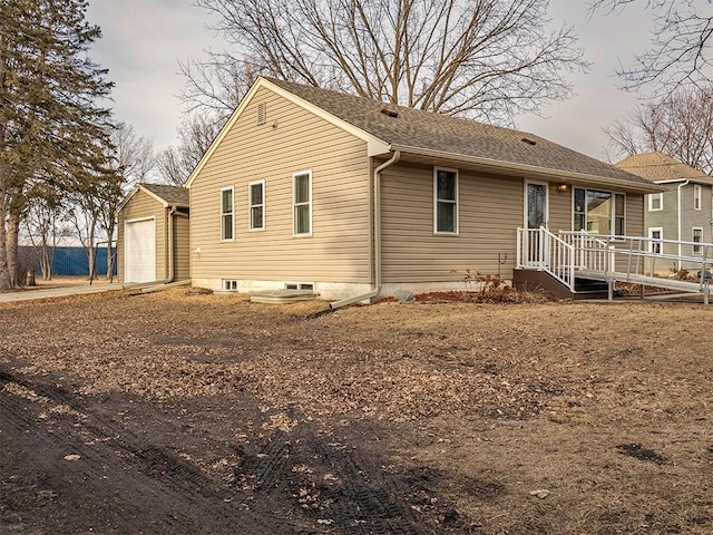 rear view of property with a garage, a shingled roof, and an outbuilding