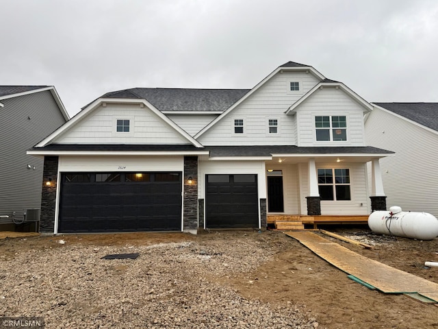 view of front facade featuring dirt driveway, a shingled roof, covered porch, a garage, and stone siding