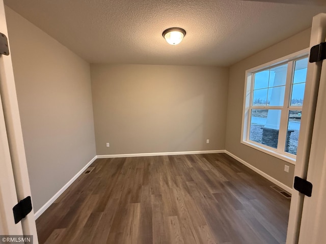 empty room with dark wood finished floors, visible vents, and baseboards