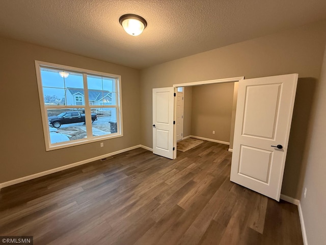 unfurnished bedroom with dark wood-style floors, baseboards, visible vents, and a textured ceiling