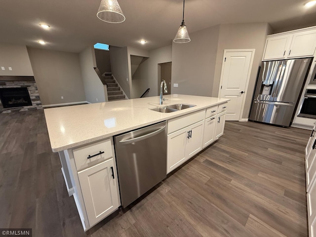 kitchen with a fireplace, stainless steel appliances, dark wood-type flooring, white cabinetry, and a sink