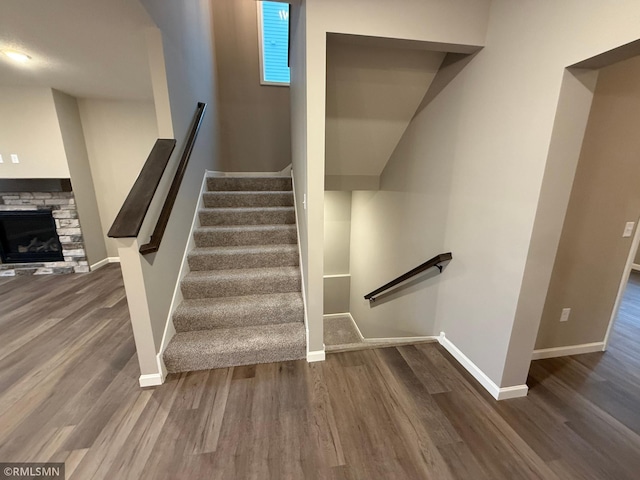 stairway with a stone fireplace, wood finished floors, and baseboards