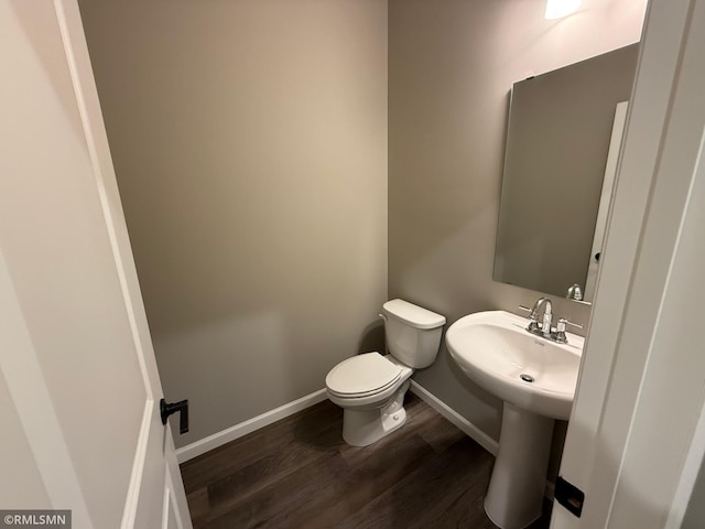 half bathroom with toilet, a sink, baseboards, and wood finished floors