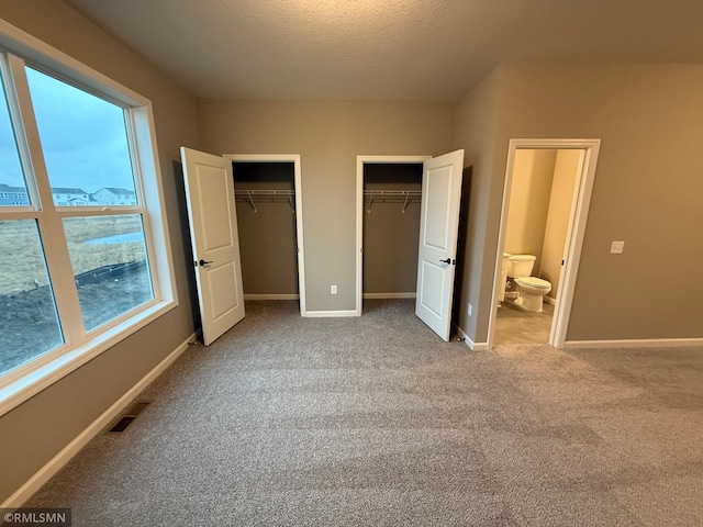 unfurnished bedroom with visible vents, baseboards, a textured ceiling, carpet floors, and two closets