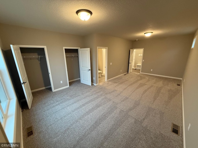 unfurnished bedroom featuring baseboards, visible vents, connected bathroom, a textured ceiling, and two closets