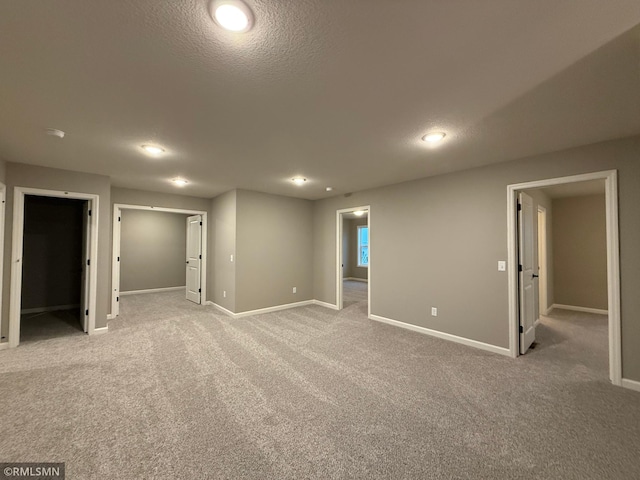 empty room featuring light carpet, a textured ceiling, and baseboards