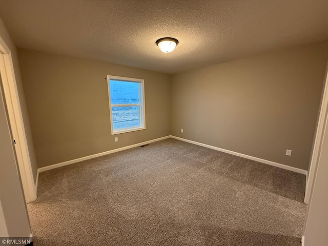 spare room with visible vents, baseboards, dark colored carpet, and a textured ceiling