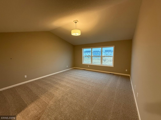 carpeted spare room featuring lofted ceiling, visible vents, and baseboards