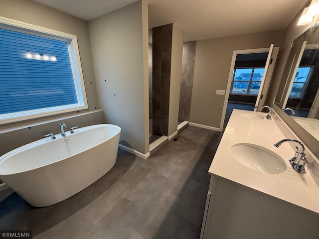 full bath featuring a freestanding tub, baseboards, a tile shower, and a sink