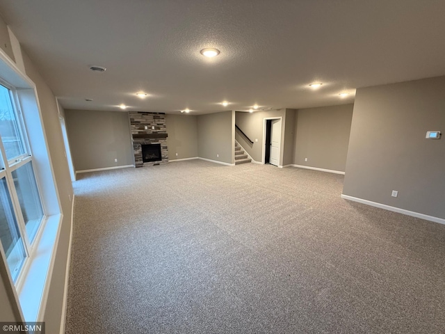 below grade area featuring a textured ceiling, a large fireplace, carpet floors, baseboards, and stairs