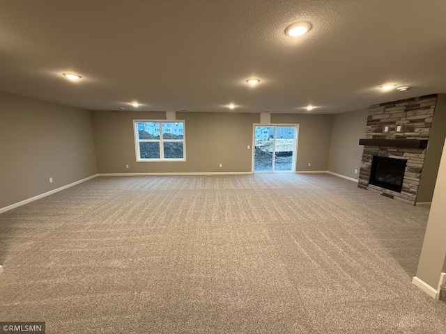 unfurnished living room featuring carpet floors, a fireplace, baseboards, and a textured ceiling