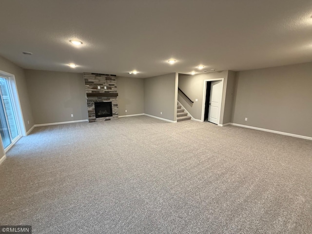 unfurnished living room featuring a stone fireplace, carpet flooring, stairway, and baseboards