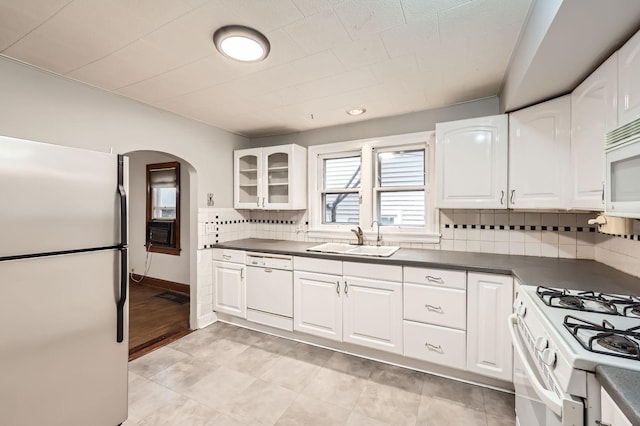 kitchen featuring arched walkways, white appliances, a sink, and dark countertops