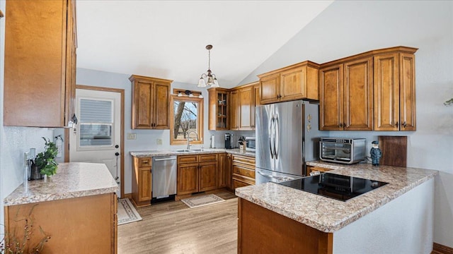 kitchen featuring stainless steel appliances, a peninsula, brown cabinetry, light wood finished floors, and vaulted ceiling