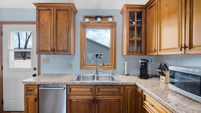 kitchen with a sink, stainless steel dishwasher, brown cabinetry, light countertops, and glass insert cabinets