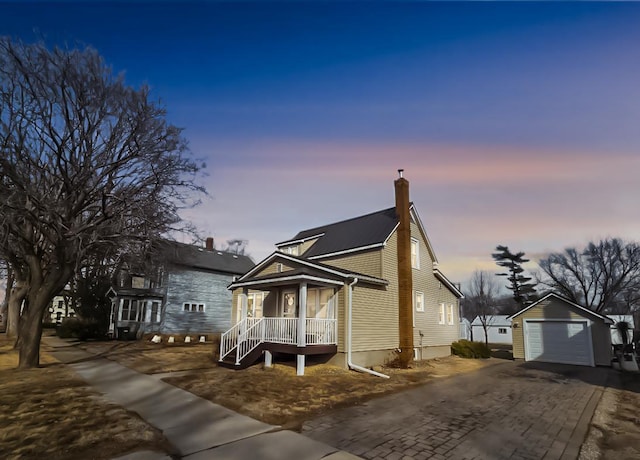 view of front of home featuring driveway, a garage, a chimney, an outbuilding, and covered porch