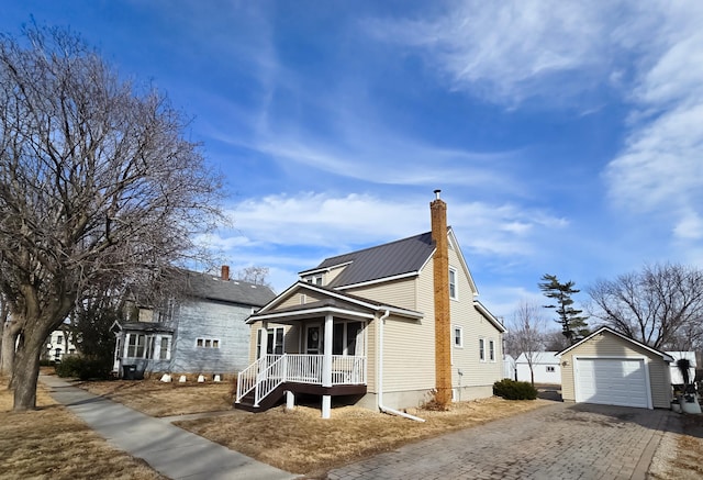 view of front of home featuring an outbuilding, aphalt driveway, covered porch, a detached garage, and a chimney