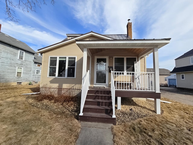 view of front of home with metal roof, a chimney, and a porch