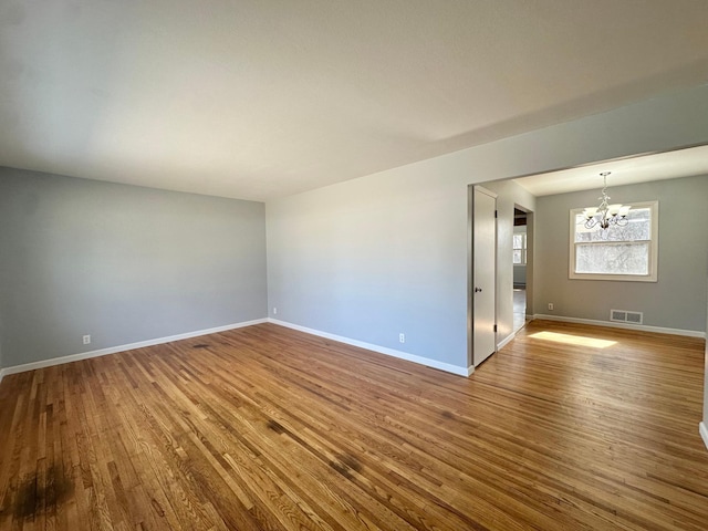 spare room with baseboards, wood finished floors, visible vents, and a chandelier