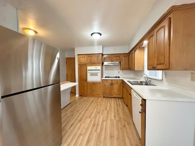 kitchen with white appliances, brown cabinets, a sink, under cabinet range hood, and light wood-type flooring