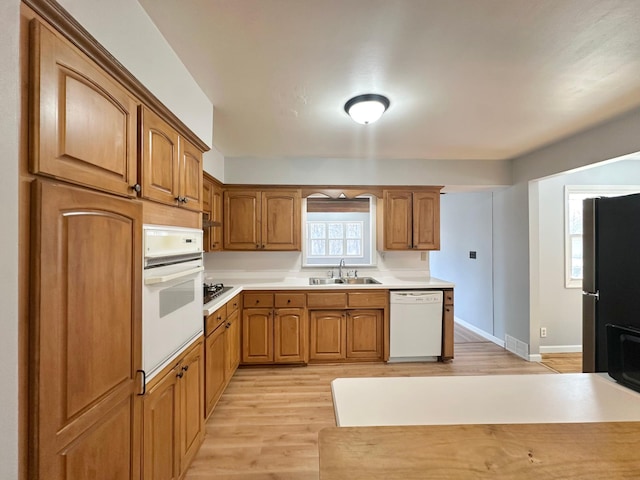 kitchen featuring white appliances, a sink, light countertops, light wood-style floors, and brown cabinets