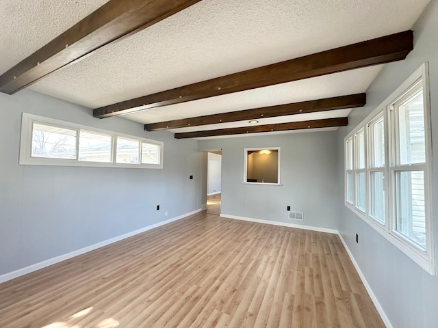 unfurnished room with baseboards, a textured ceiling, beam ceiling, and light wood-style flooring