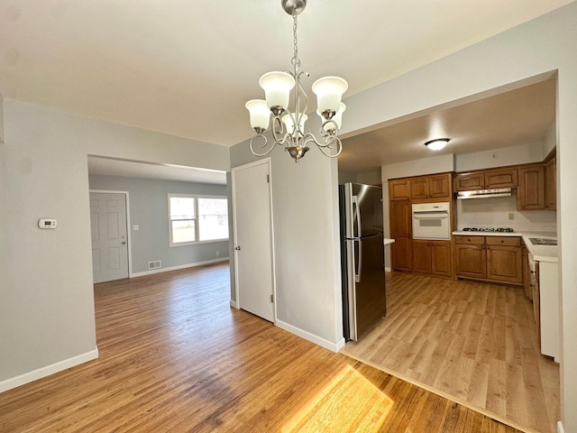 kitchen featuring freestanding refrigerator, brown cabinetry, light wood finished floors, white oven, and light countertops