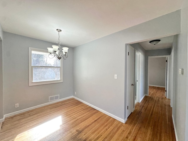 unfurnished dining area featuring a notable chandelier, visible vents, baseboards, and wood finished floors