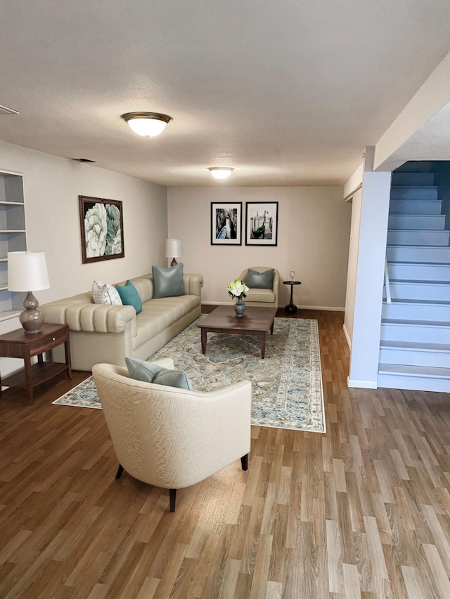 living area featuring stairway, a textured ceiling, baseboards, and wood finished floors