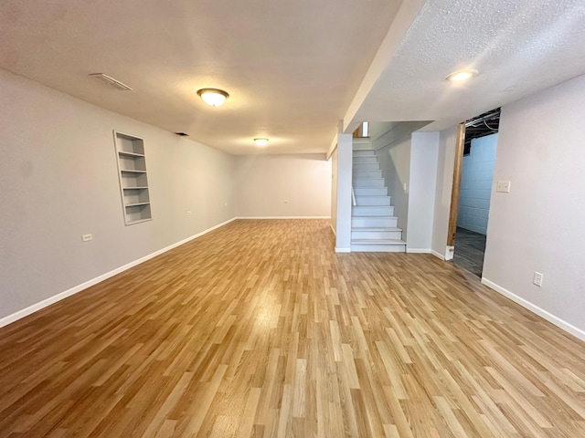 finished basement with a textured ceiling, stairs, baseboards, and wood finished floors