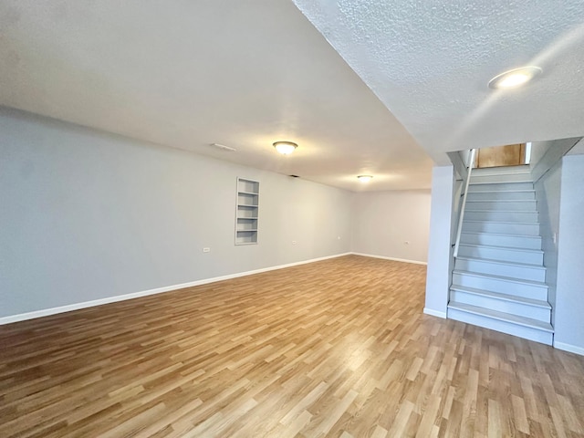 finished below grade area with built in features, a textured ceiling, baseboards, and wood finished floors