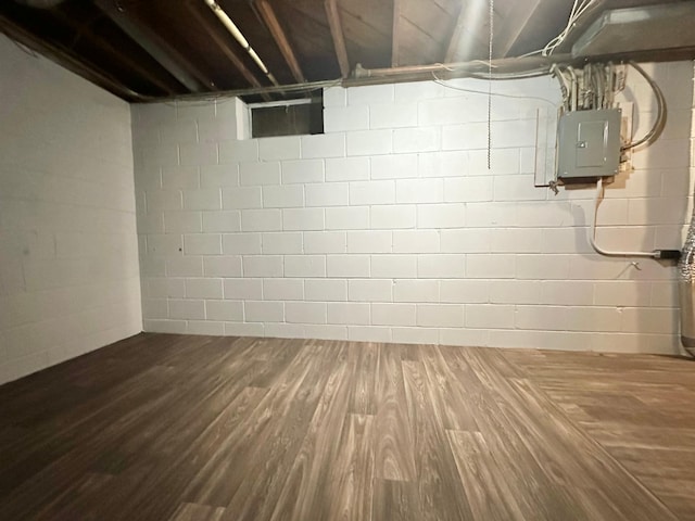 unfinished basement with concrete block wall, electric panel, and wood finished floors