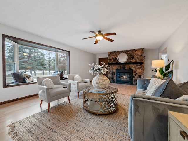 living room with a ceiling fan, a fireplace, light wood-type flooring, and baseboards