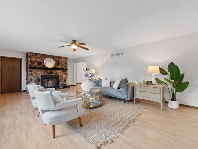 living area with a fireplace, wood finished floors, visible vents, and ceiling fan