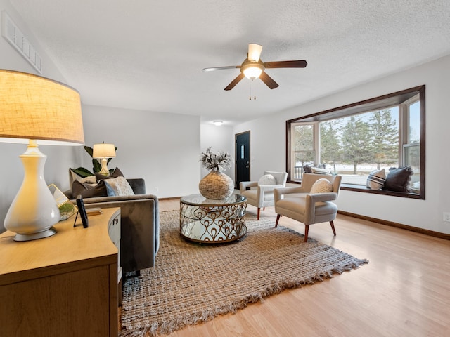 living room featuring visible vents, a ceiling fan, a textured ceiling, wood finished floors, and baseboards