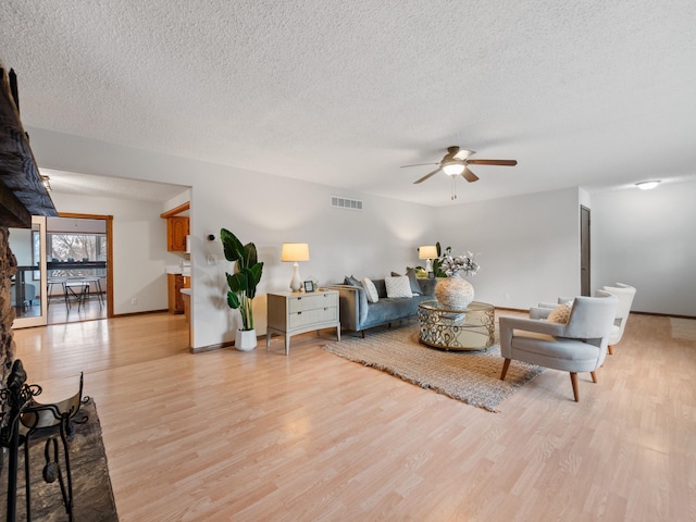 living area with light wood finished floors, visible vents, a textured ceiling, and ceiling fan