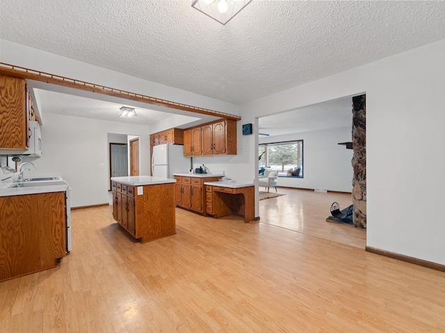 kitchen featuring light wood-type flooring, brown cabinets, a sink, a kitchen island, and freestanding refrigerator