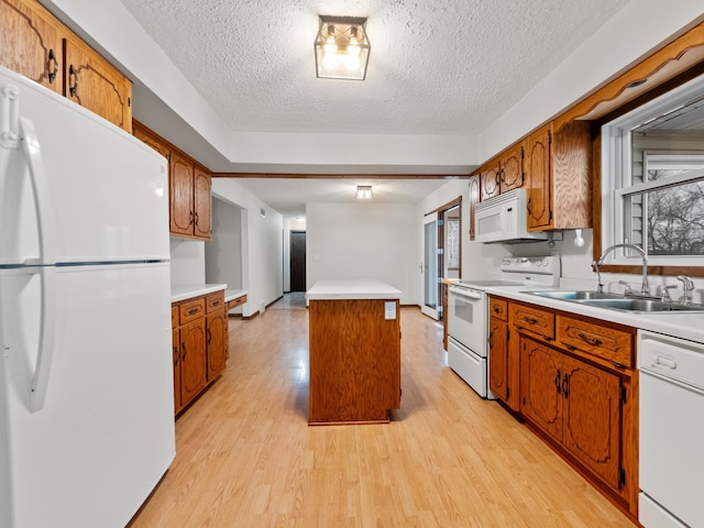 kitchen with white appliances, a sink, light countertops, light wood-style floors, and a center island