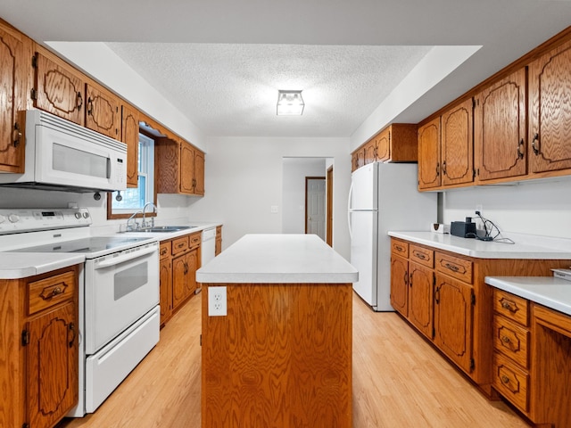 kitchen with light wood-style flooring, a sink, a kitchen island, white appliances, and brown cabinetry