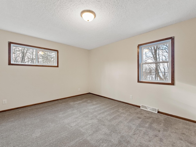 carpeted spare room with baseboards, visible vents, and a textured ceiling