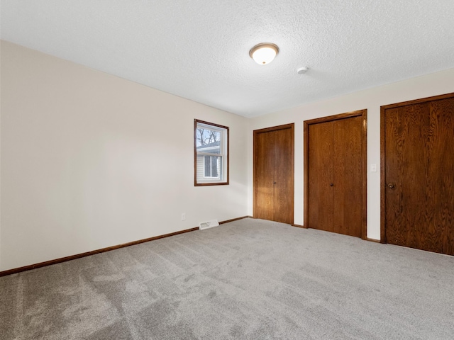 unfurnished bedroom featuring carpet, baseboards, visible vents, multiple closets, and a textured ceiling