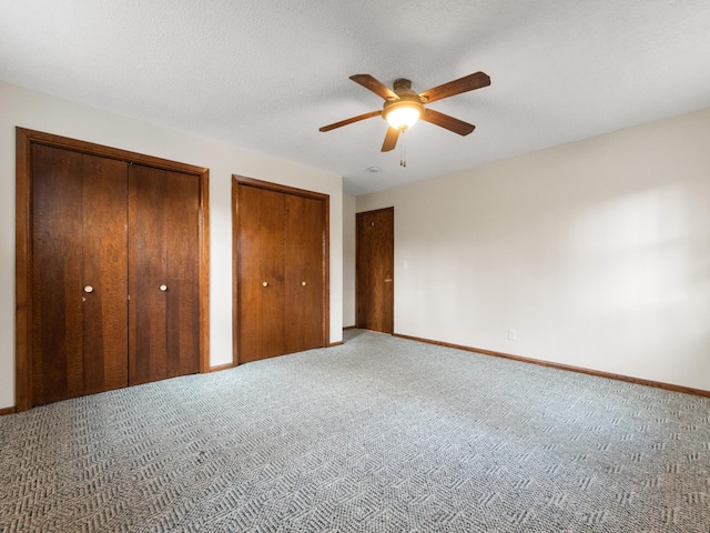 unfurnished bedroom with baseboards, ceiling fan, a textured ceiling, carpet flooring, and two closets