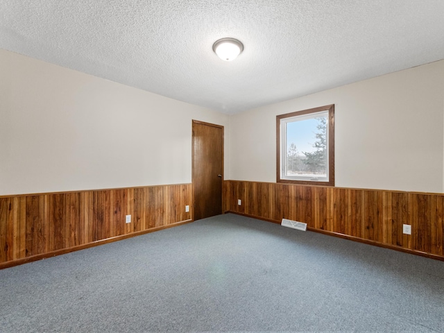 unfurnished room featuring visible vents, wainscoting, a textured ceiling, and wood walls