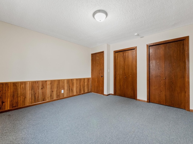 unfurnished bedroom with wooden walls, multiple closets, a wainscoted wall, carpet floors, and a textured ceiling