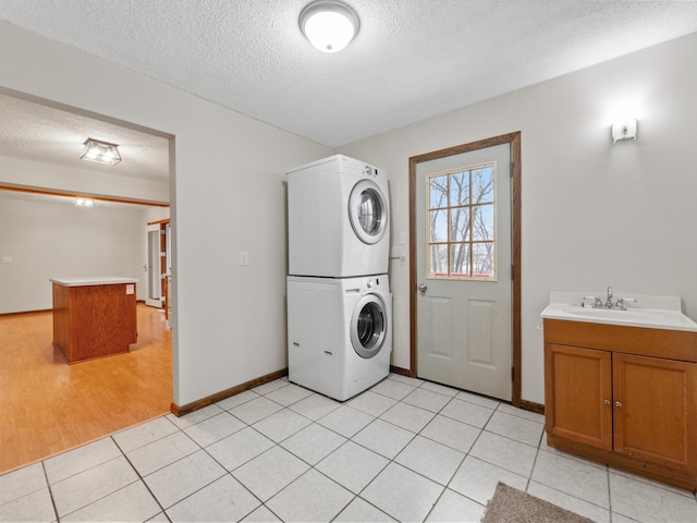 laundry room featuring baseboards, light tile patterned floors, stacked washer and clothes dryer, a textured ceiling, and a sink